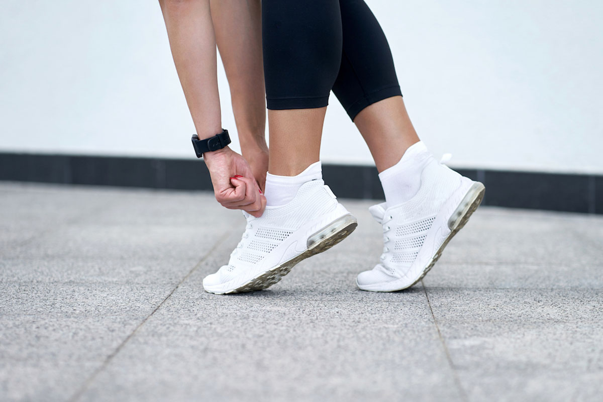 Closeup of female legs in black sport leggings in stylish white sneakers. Active slim woman on a training. Ready to start.